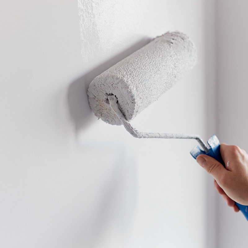 Main tenant un rouleau appliquant de la peinture blanche sur un mur, laissant une trace fraîche et humide.