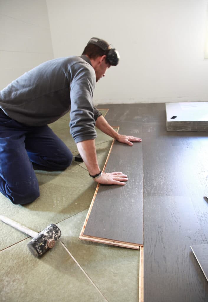 Un homme pose du parquet gris foncé sur une sous-couche verte. Il est à genoux et ajuste la planche à la main.